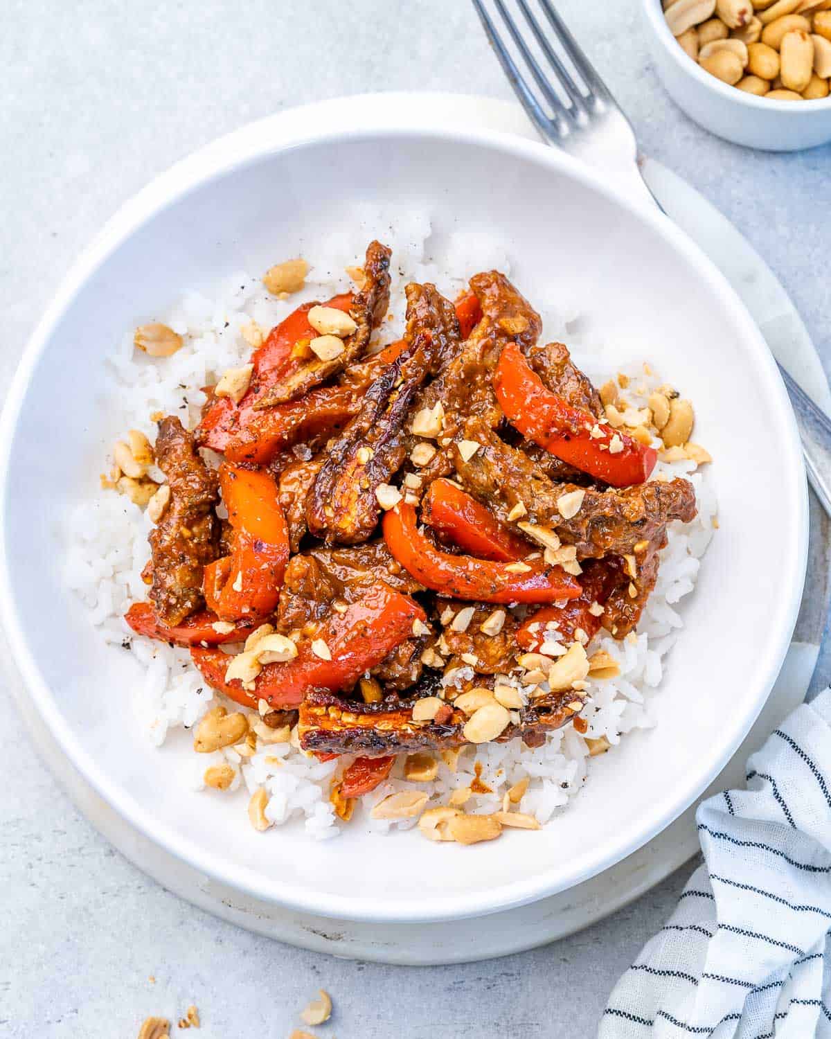 Kung pao beef over white rice in a white bowl.