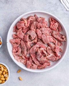 Thinly sliced pieces of uncooked beef strips on a white plate.