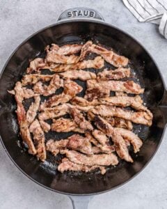 Cooking flank steak strips in a skillet.