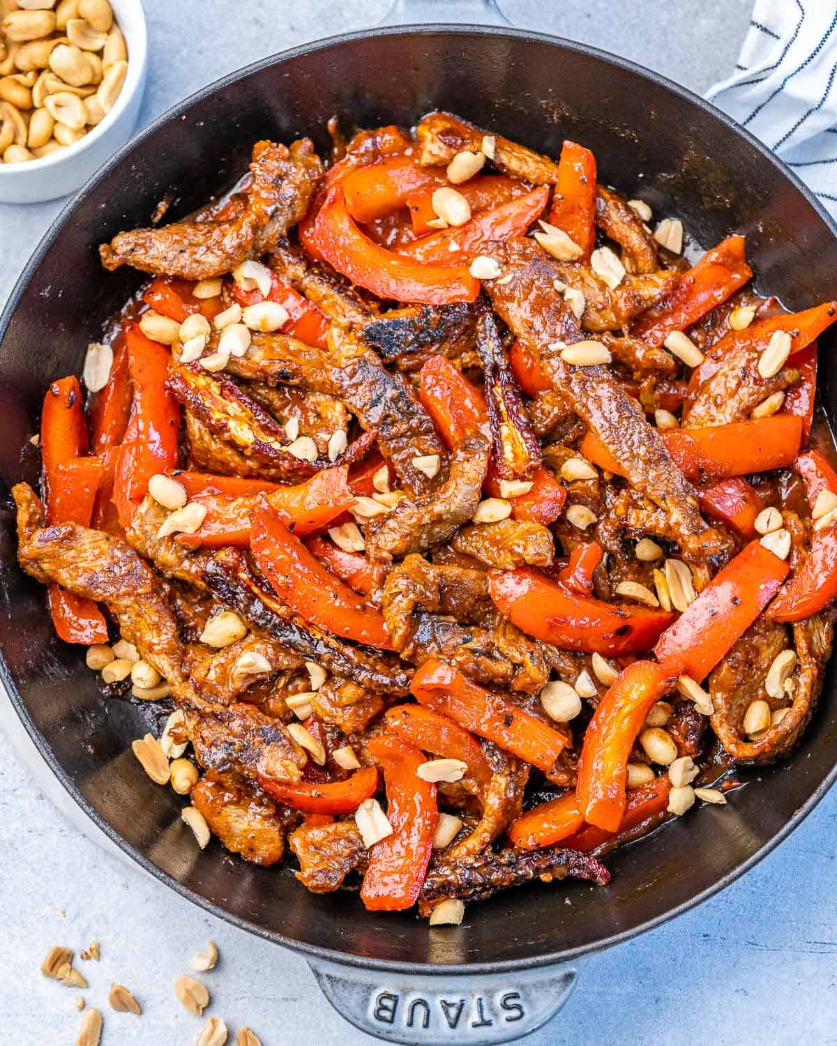 Red bell peppers cooking with steak in a skillet.