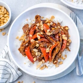 white bowl with rice and sauteed kung pao beef with red bell pepper.