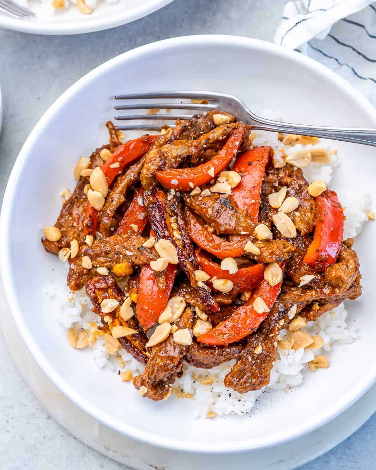 Kung pao beef with a fork over white rice in a white bowl.