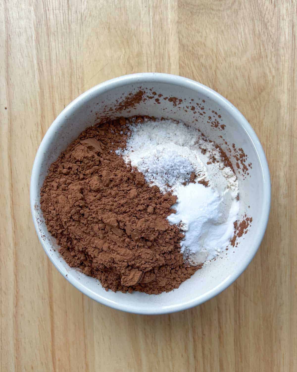 Flour, cocoa powder, salt, and baking soda are added to a bowl.