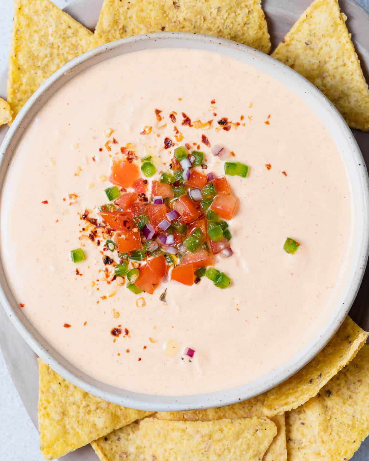 Cottage cheese queso garnished with chopped tomato and jalapeños and surrounded by tortilla chips.
