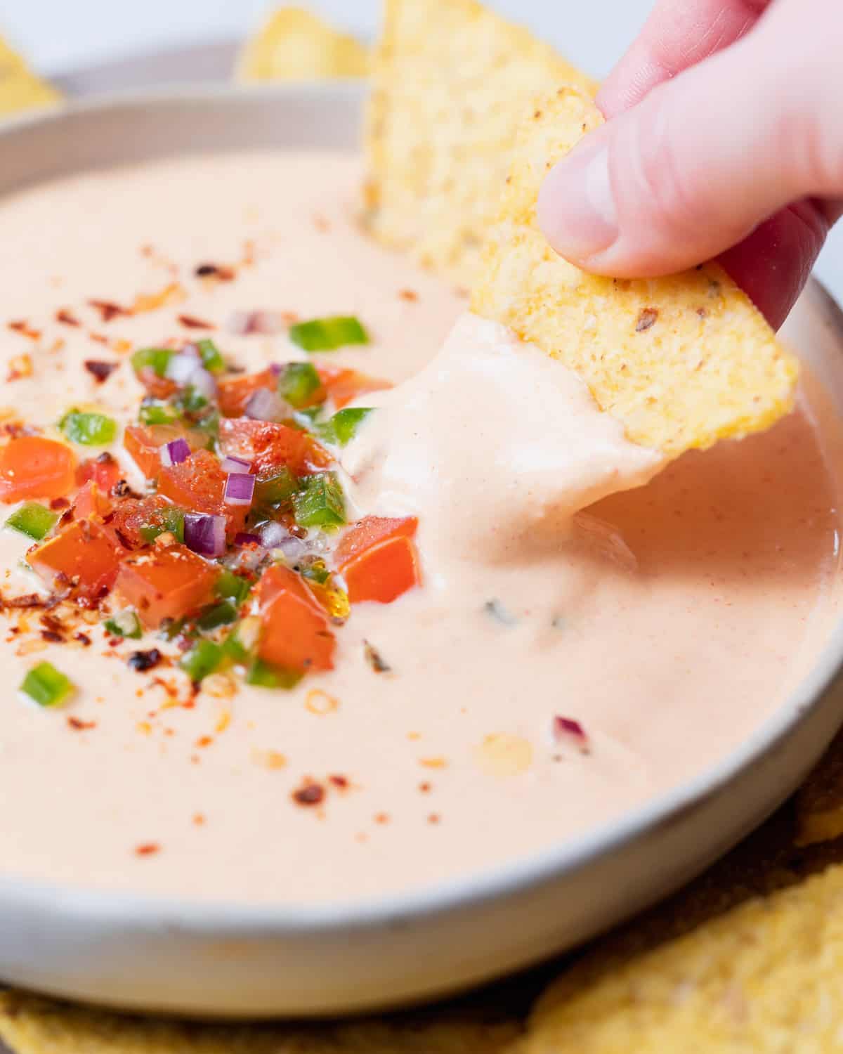 Hand dipping a chip into a cheese dip.