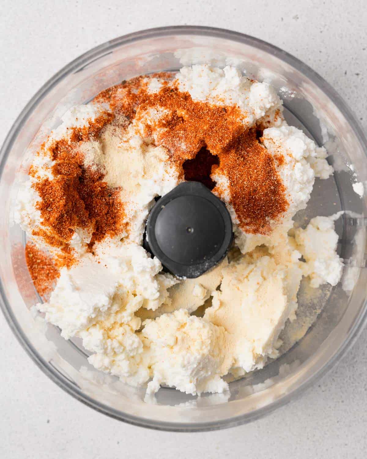 Cottage cheese in a food processor with seasonings on top.