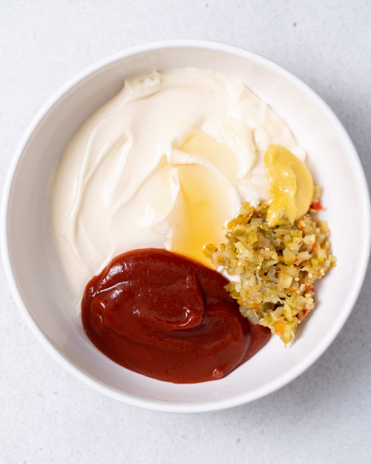 Ketchup, honey, mayo and pickle relish in a white bowl.