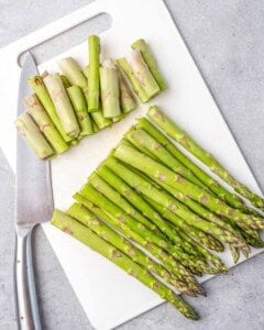 trimming the stems of asparagus on a cutting board.
