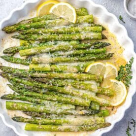 baked asparagus topped with parmesan cheese and lemon garnishes.