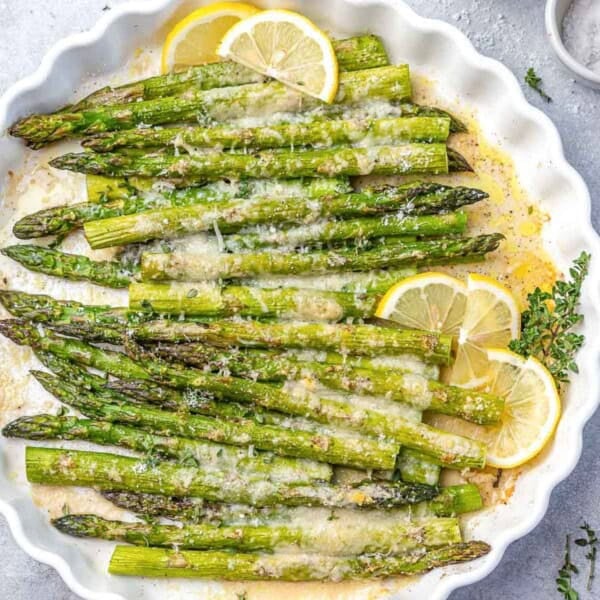 baked asparagus topped with parmesan cheese and lemon garnishes.