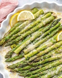 baked and seasoned asparagus in a dish with lemon slice garnish.