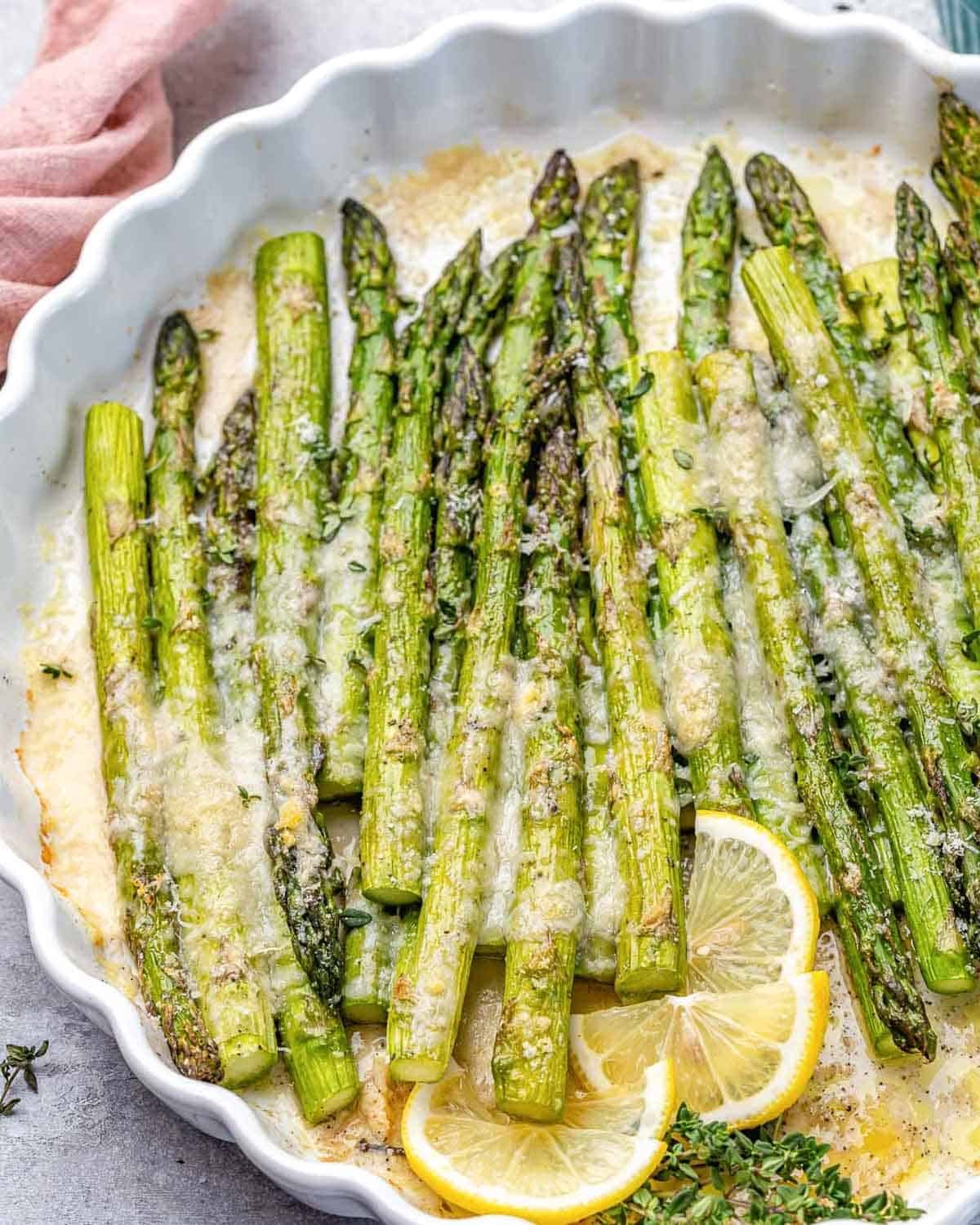 a dish with baked asparagus topped with parmesan cheese and lemon garnish.