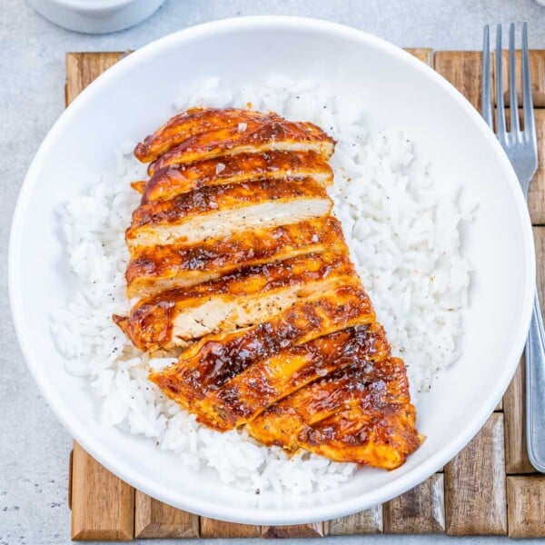 a round white bowl with sliced bbq chicken breast over white rice.