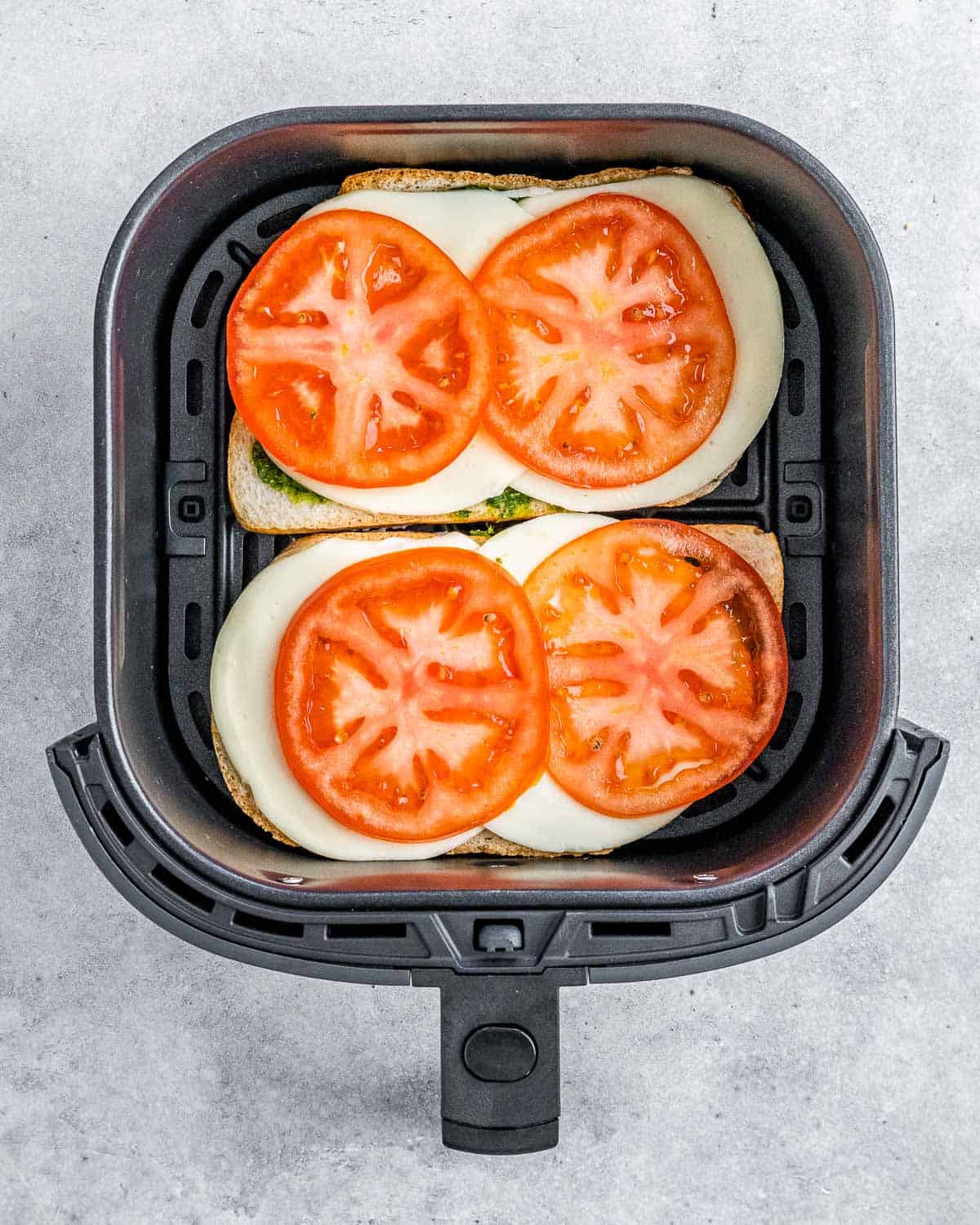 Sandwich bread in an air fryer topped with sliced tomato.