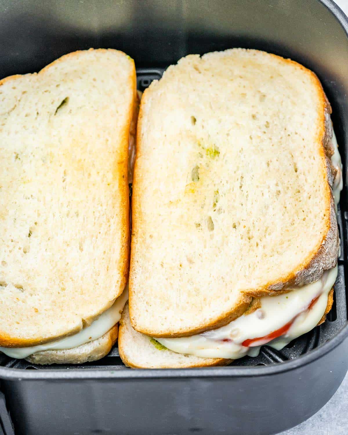 Cheese and tomato sandwich cooking in an air fryer.