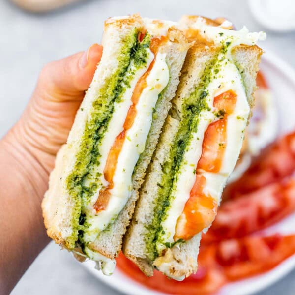 hand holding 2 halved grilled cheese with pesto and tomatoes.