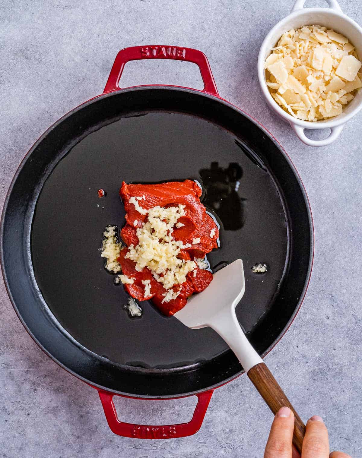 Stirring tomato paste and garlic in a skillet.