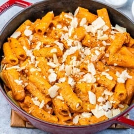 creamy tomato base pasta in a red skillet topped with shredded cheese.