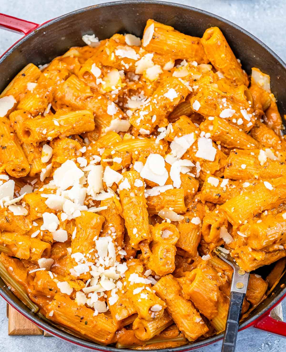 Creamy tomato base pasta in a red skillet topped with shredded cheese.