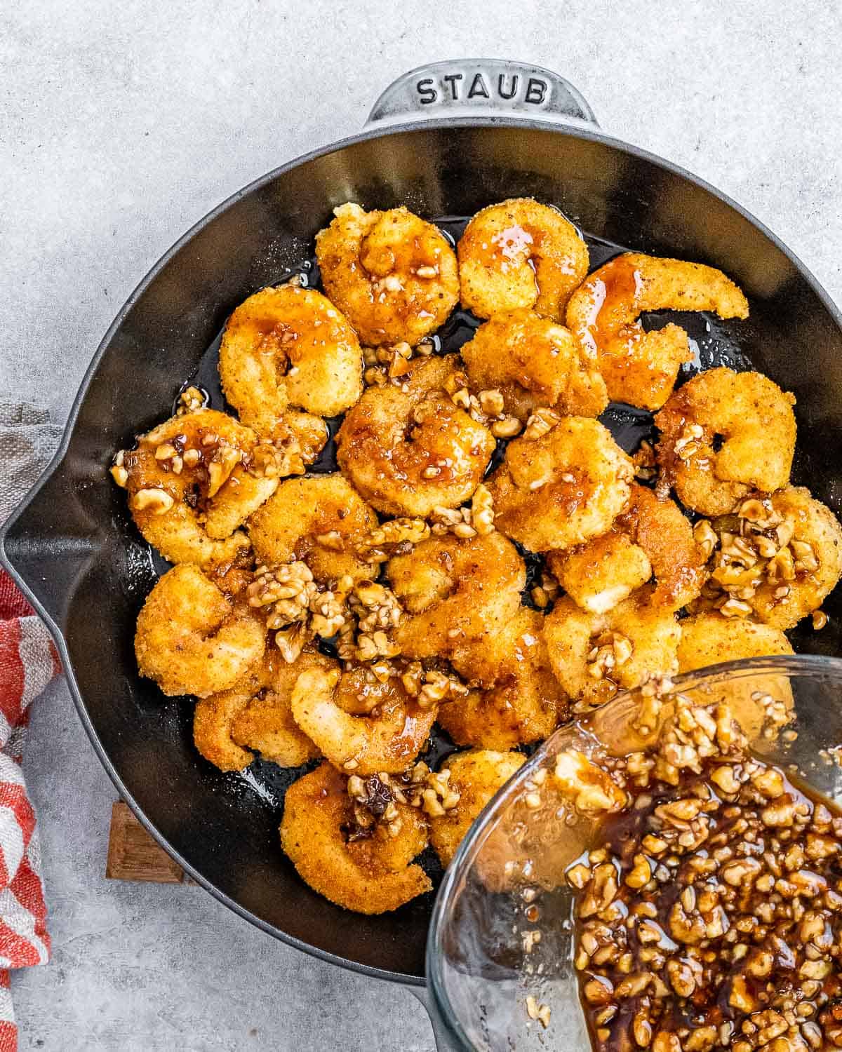 Adding sauce and walnuts to shrimp cooking in a skillet.