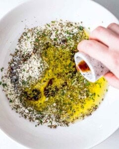adding vinegar with oil to all the seasonings in the bowl.