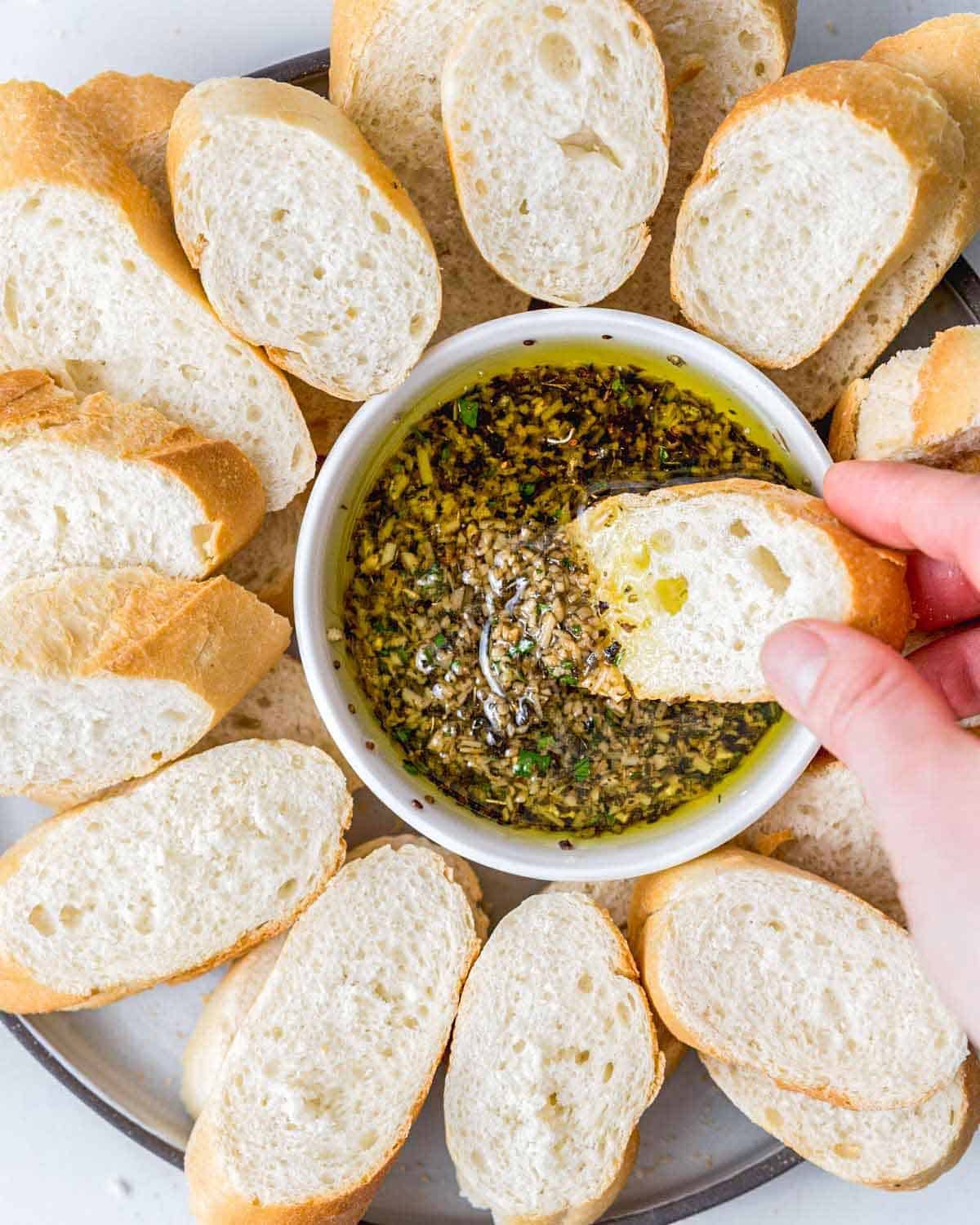 hand holding a piece of bread being dipped in olive oil bread dip.