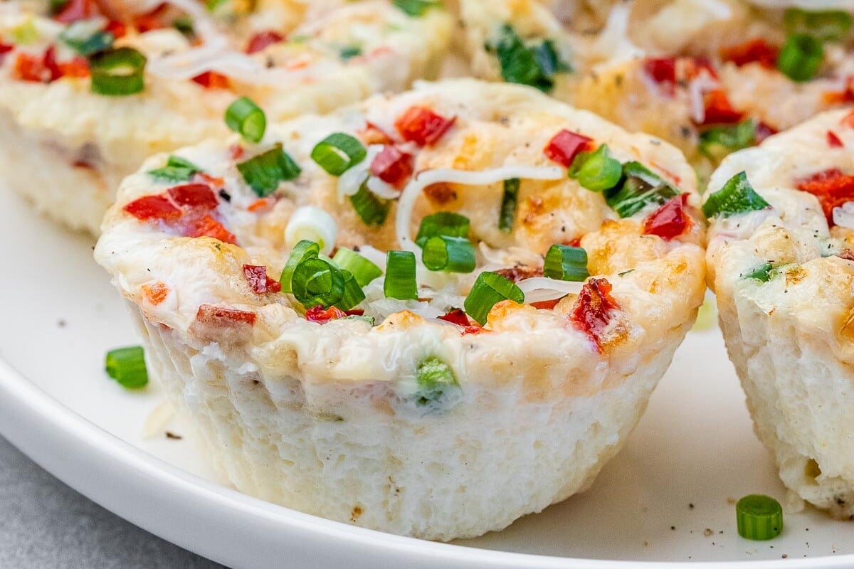 Side angle of a plate full of egg white bites, one slightly bitten to show the cheesy interior and airy texture.