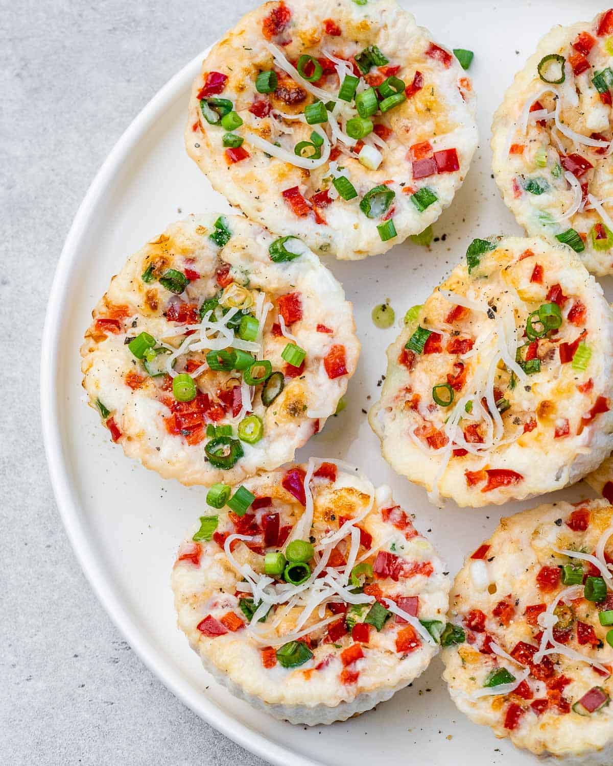Close-up shot of egg white bites on a white plate, showing the fluffy texture and colorful veggie toppings.