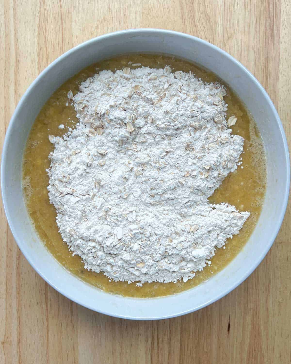 dry flour ingredients added over the eggs and banana mixture in a round bowl.