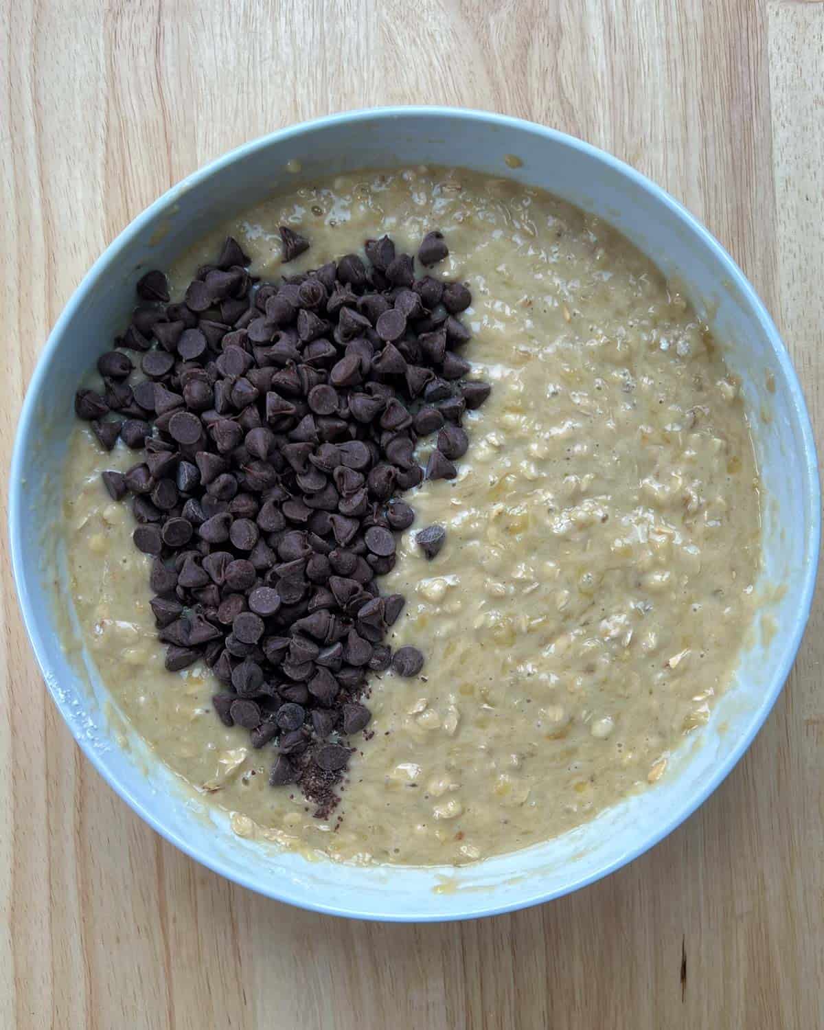 chocolate chips are added to the banana bread batter in a round bowl.