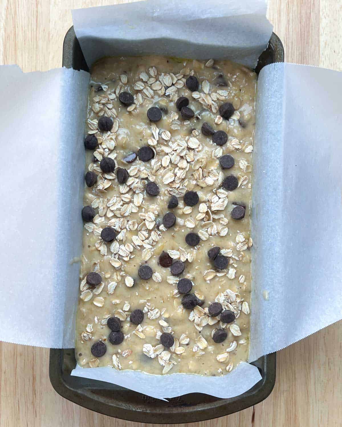 banana bread batter in a pan topped with chocolate chips and oats.