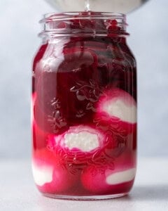 Mason jar with peeled hard-boiled eggs submerged in deep red beet pickling brine, showing the eggs starting to take on color.
