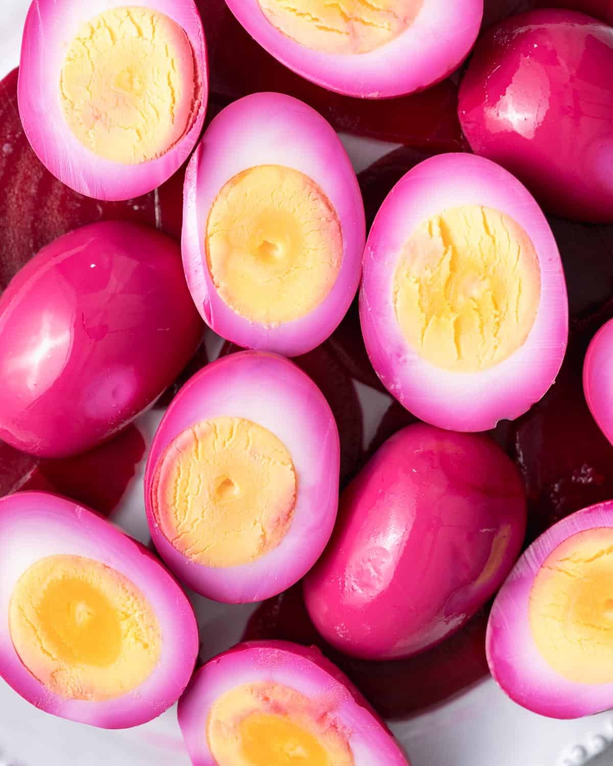 Overhead view of pink pickled egg halves and wholes with a deep pink exterior and bright orange-yellow yolks.