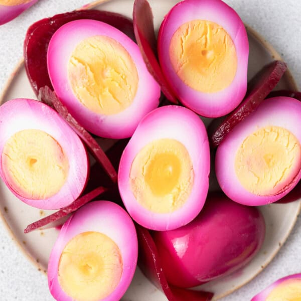A plate with pickled egg halves and sliced pickled beets on a round plate.