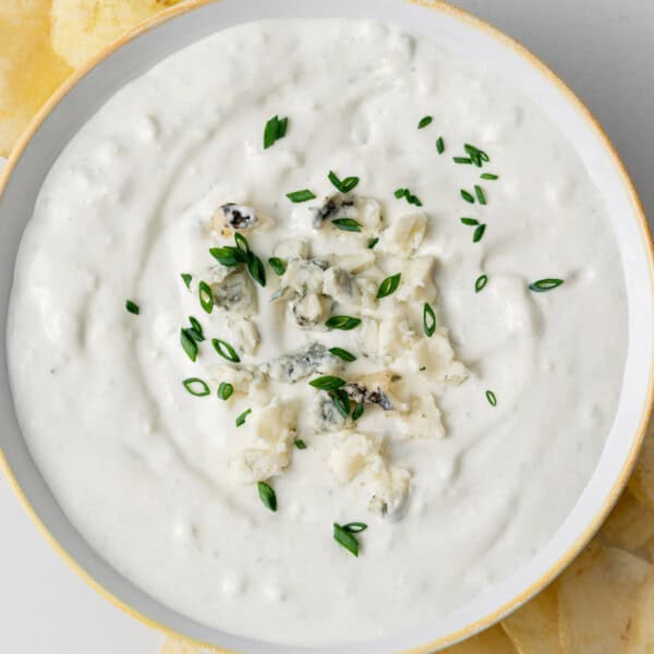 a round bowl of blue cheese dip topped with more crumbled blue cheese and sliced chives.