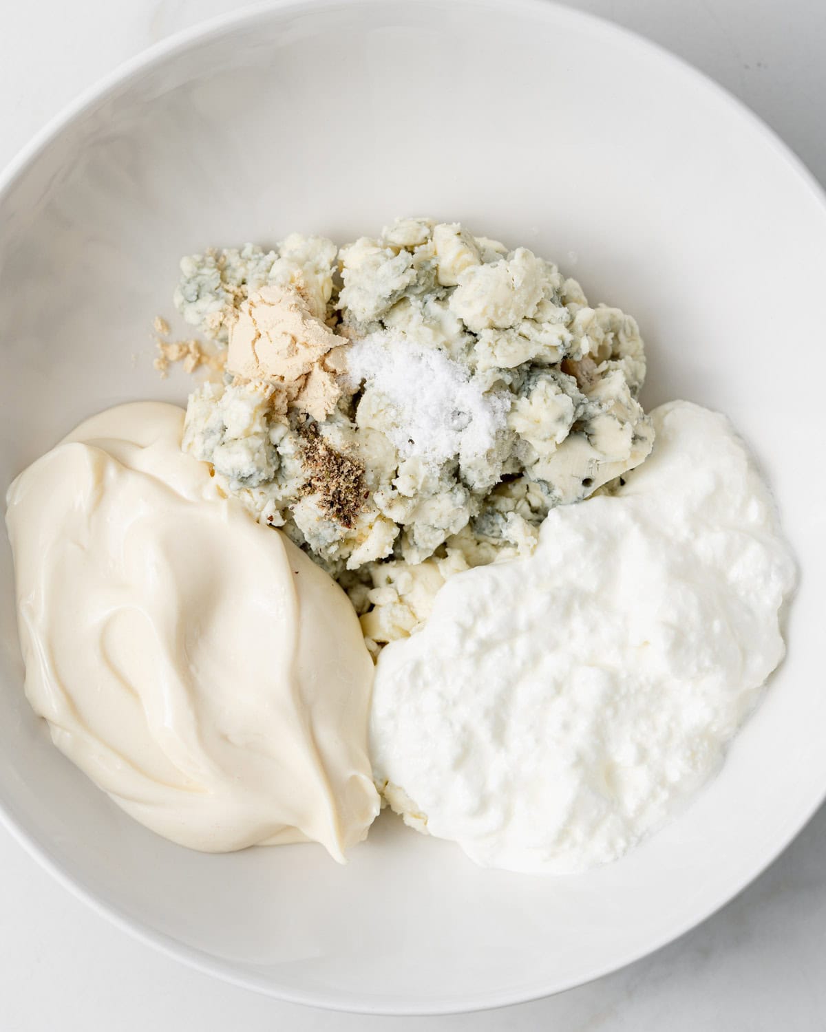 Blue cheese, mayo, sour cream and seasonings in a white bowl.