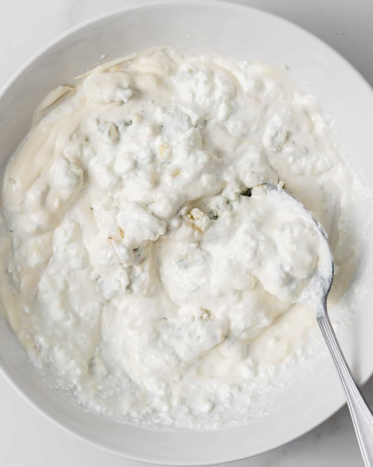 Stirring blue cheese crumbles into sour cream and mayo.