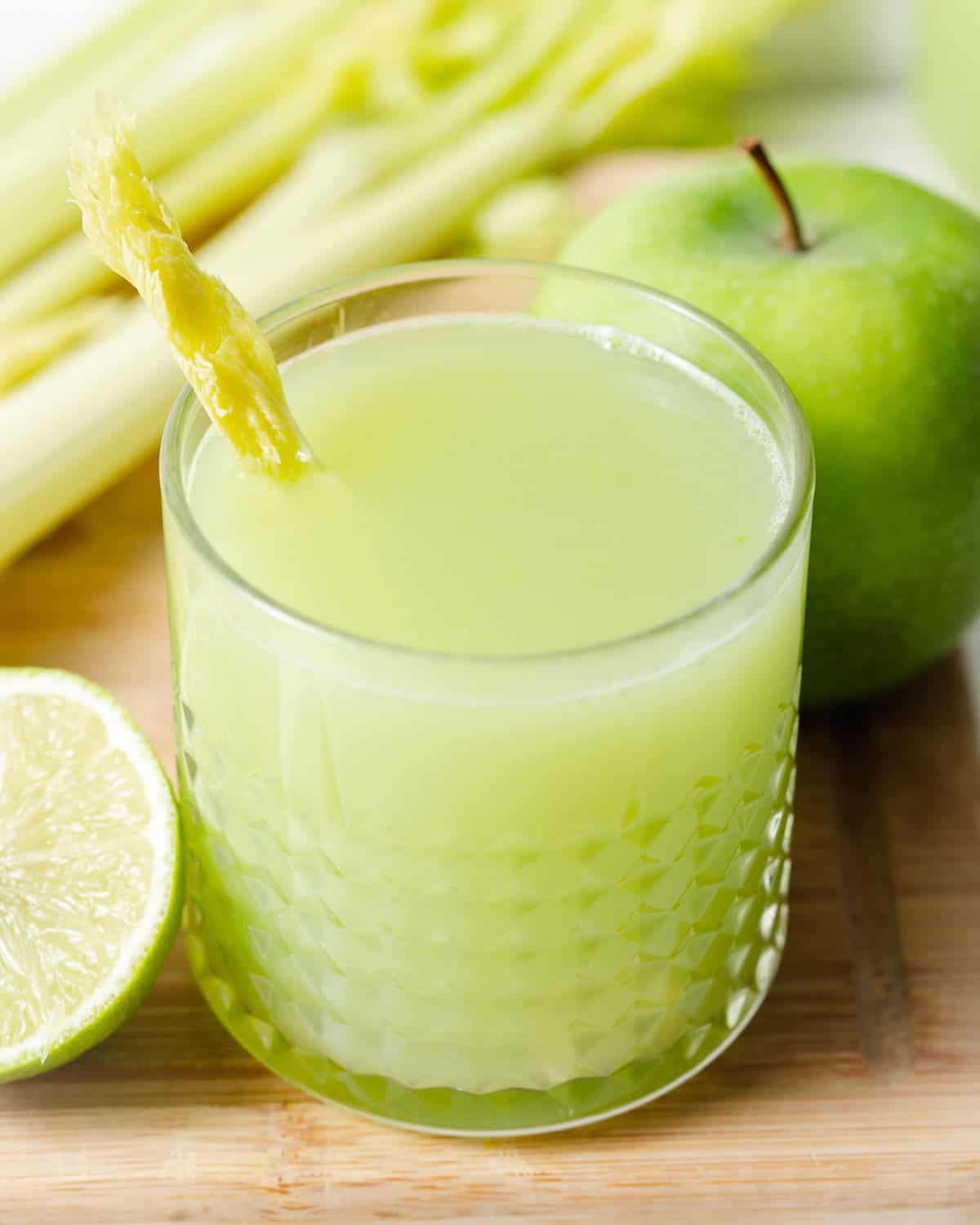 A glass of celery juice with apple and lime on a wooden board.