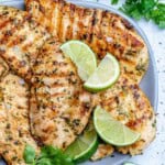 grilled chicken breast on a plate with lime wedges.