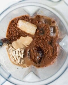 Coffee in a blender with a frozen banana, protein powder, milk and a date.