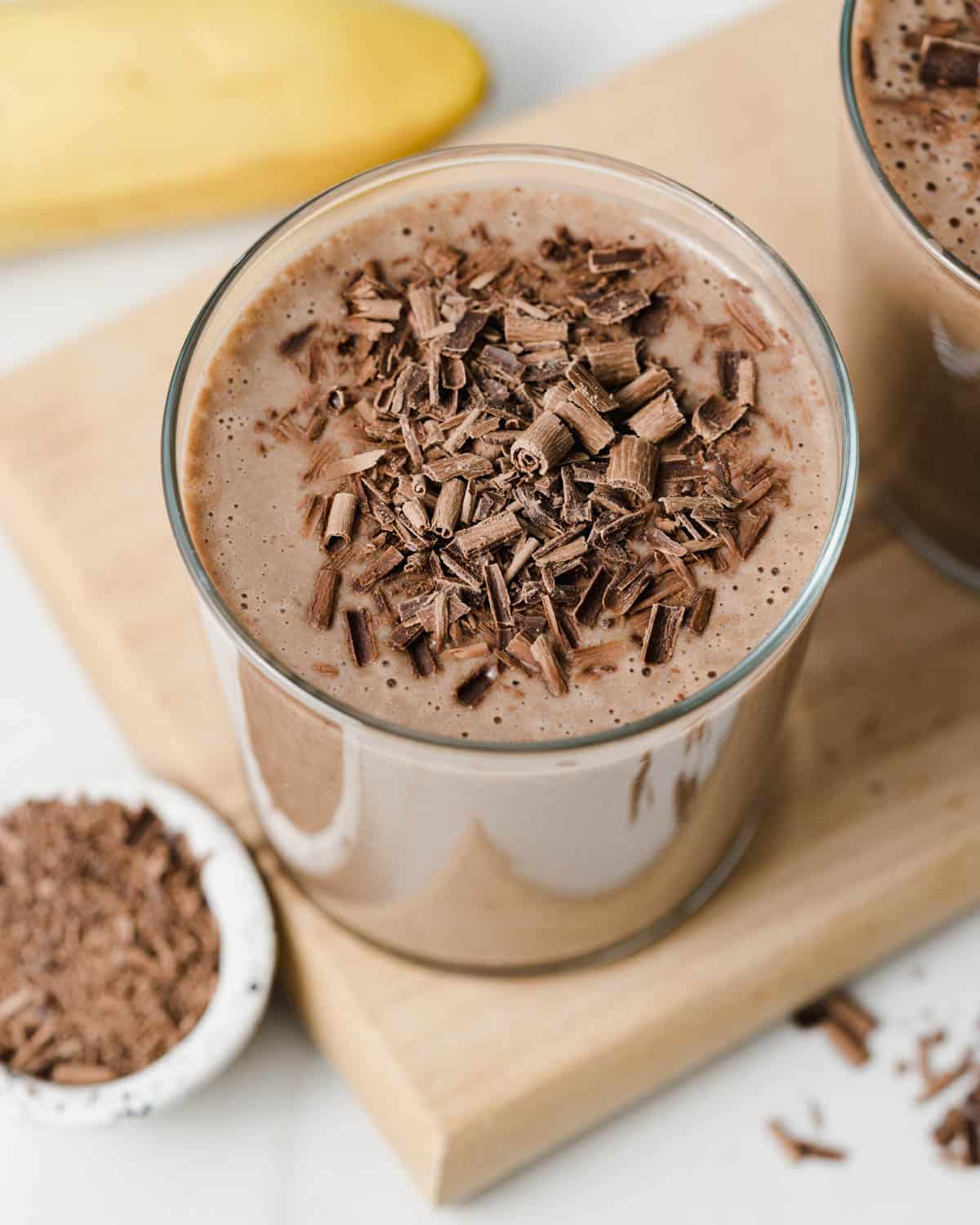 A clear cup on a cutting board filled with coffee smoothie and topped with shaved chocolate.