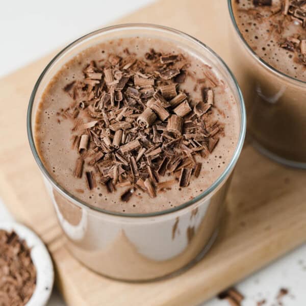 A clear cup on a cutting board filled with coffee smoothie and topped with shaved chocolate.