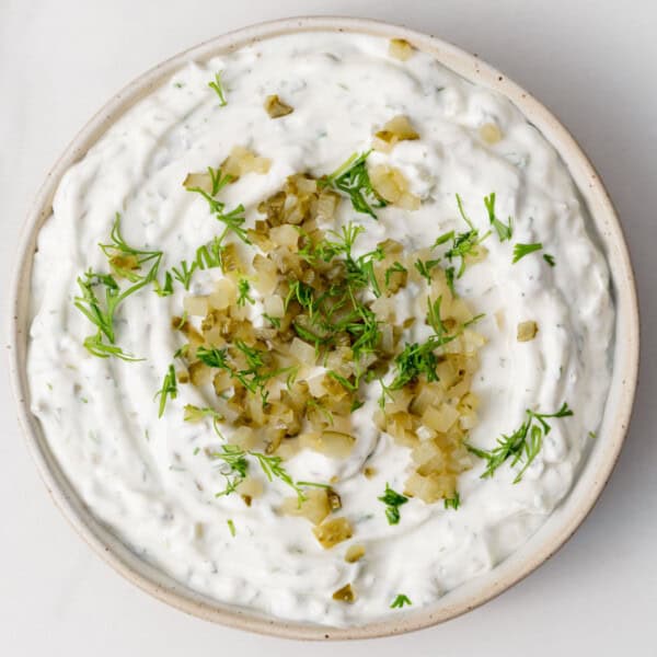a round bowl full of yogurt base pickle dip topped with chopped pickles and herbs.