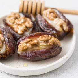 4 stuffed dates with goat cheese and walnuts drizzled with honey on a plate.