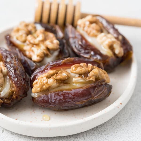 4 stuffed dates with goat cheese and walnuts drizzled with honey on a plate.