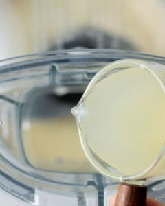 lemon juice being added into the food processor with garlic.