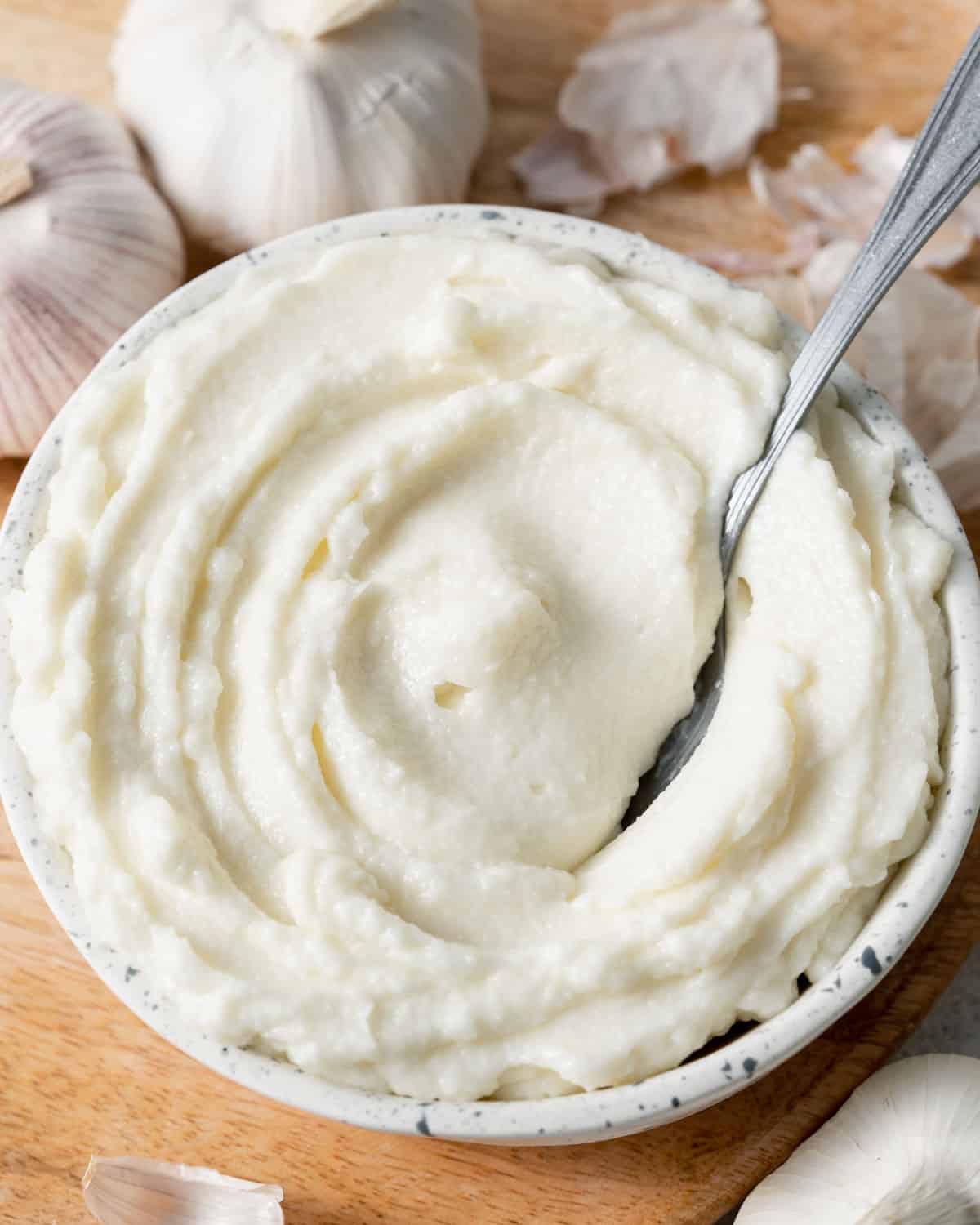 a bowl of white garlic sauce with a spoon in it.