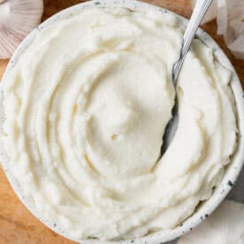 a round bowl with fluffy garlic sauce dip with a spoon in it.