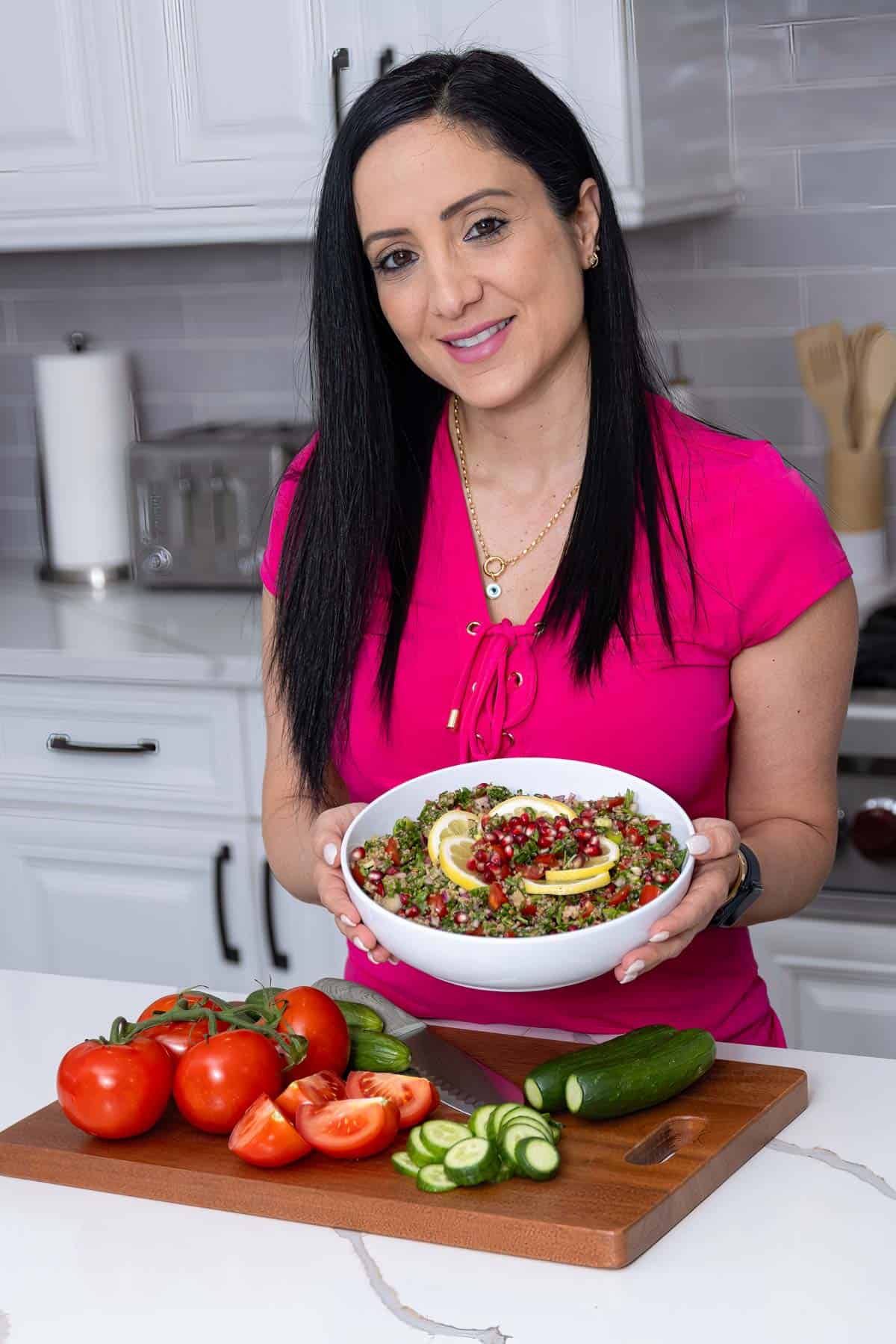 rena in a pink shirt holding a white bowl that has tabbouleh.