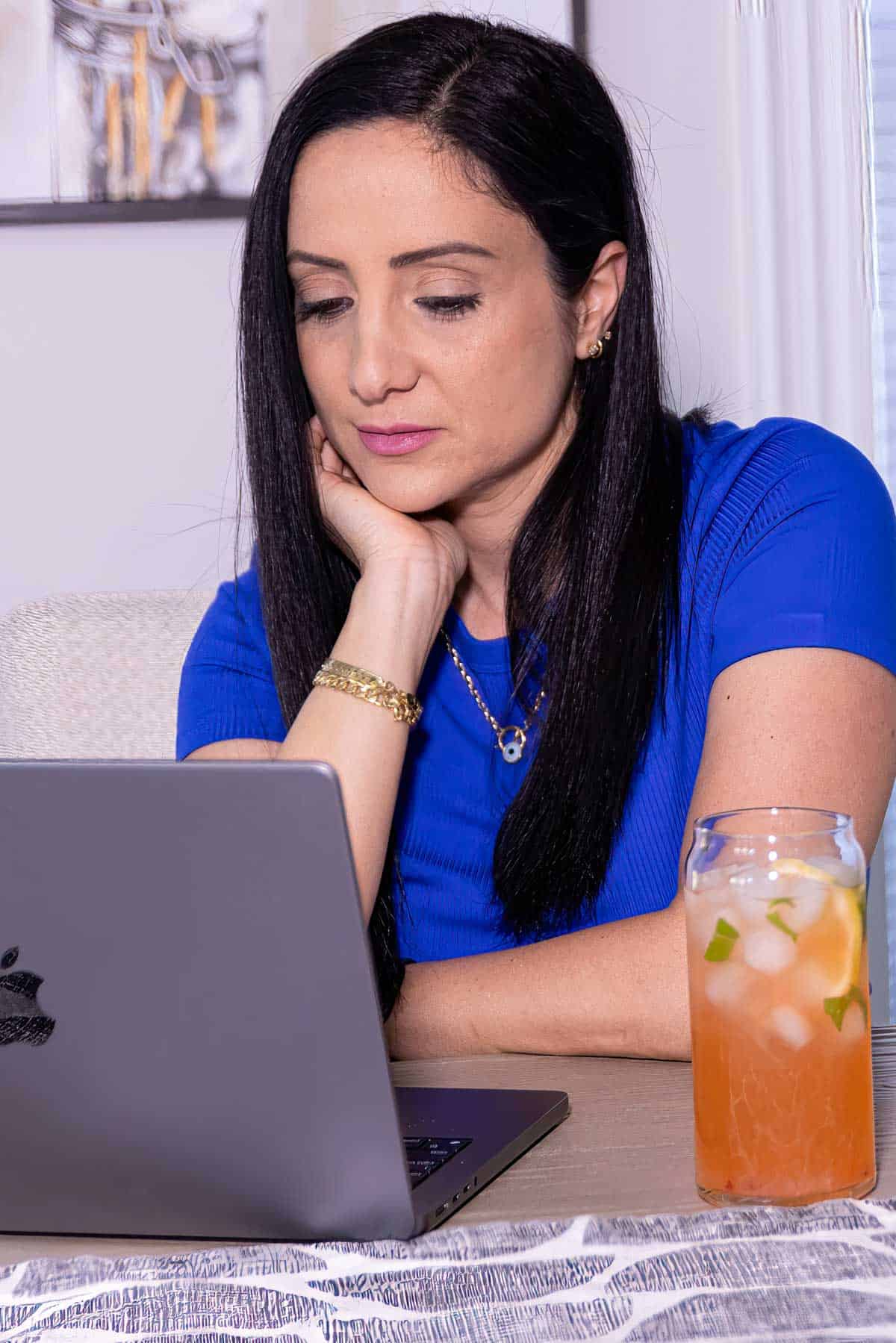 rena in a blue shirt looking down at laptop.